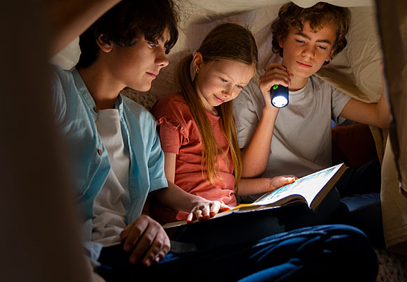 Children reading under a blanket fort with flashlight