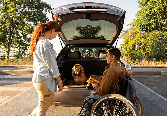 A woman, a man in wheelchair, and a dog at back of car with hatch open